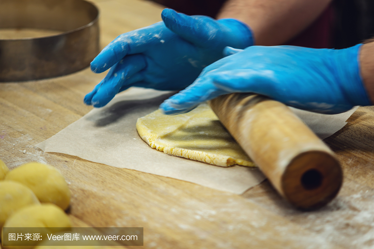 戴手套的糕点师擀面团做饼干。生产糖果